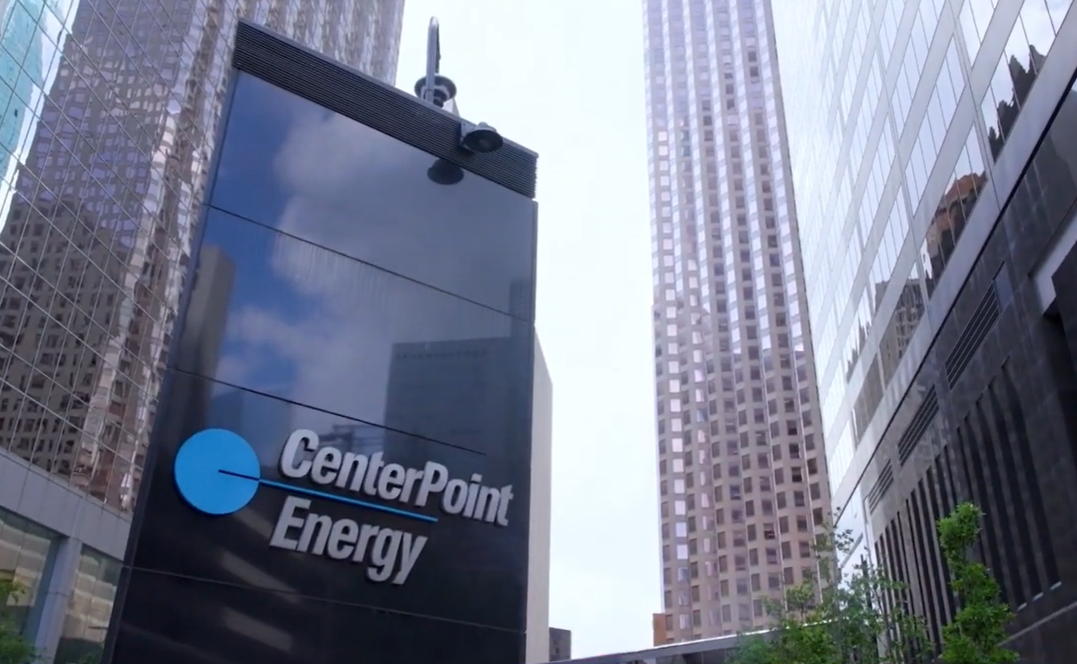A glass building with the CenterPoint Energy logo and name reflects the sky, surrounded by tall skyscrapers in a cityscape.