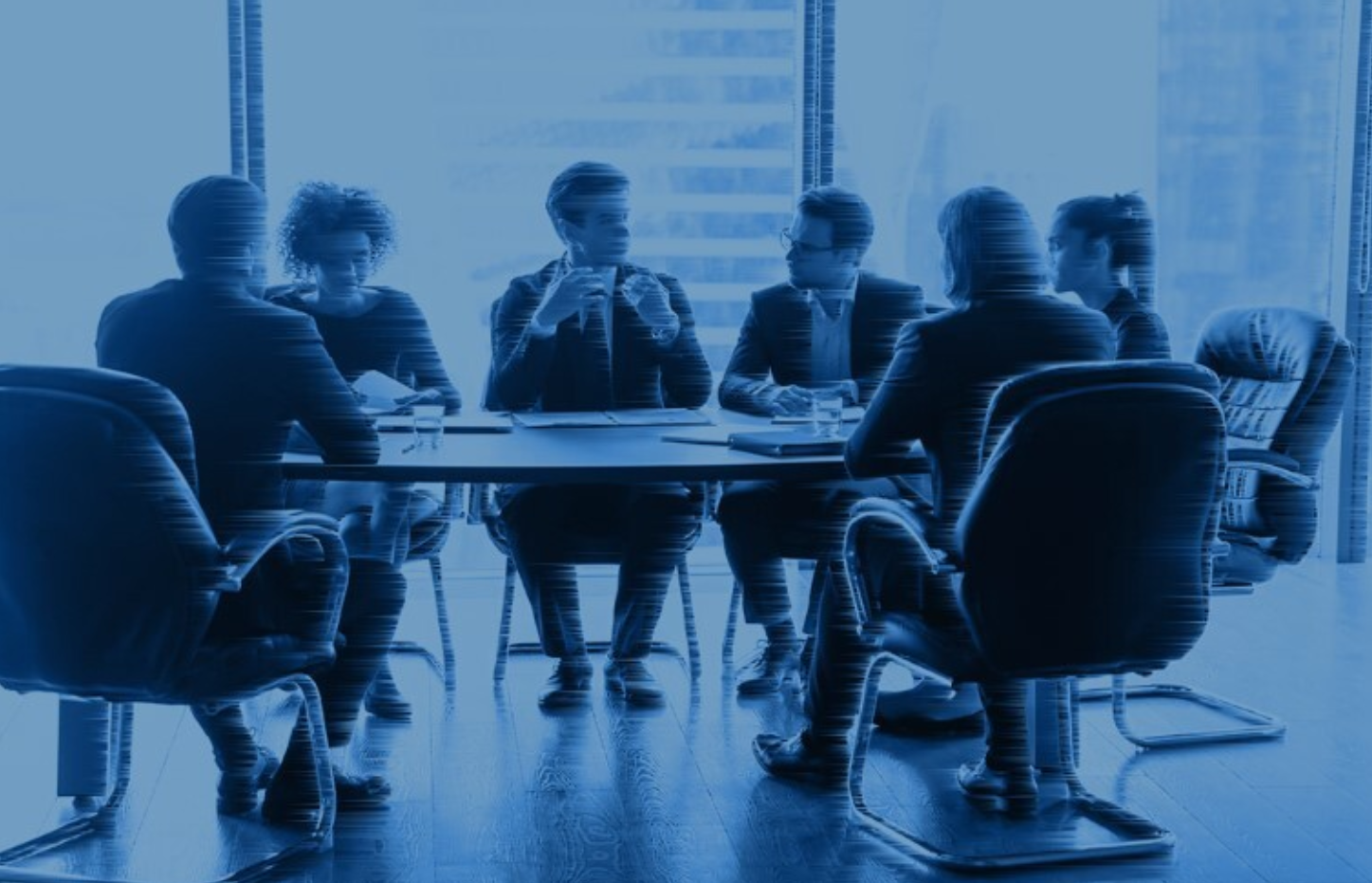Seven people in business attire sit around a conference table, engaged in discussion, in a modern office with large windows. The image has a blue overlay.