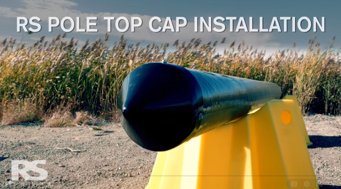 A black pole top cap is installed on a yellow barrier outdoors, with grass and sky in the background. Text reads, RS POLE TOP CAP INSTALL..